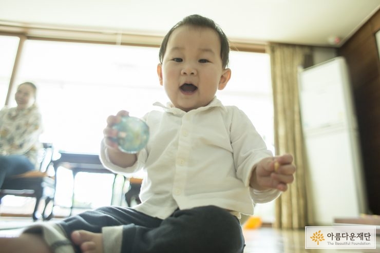 공을 든 아이가 바닥에 앉아 카메라를 내려다 보고 있다.